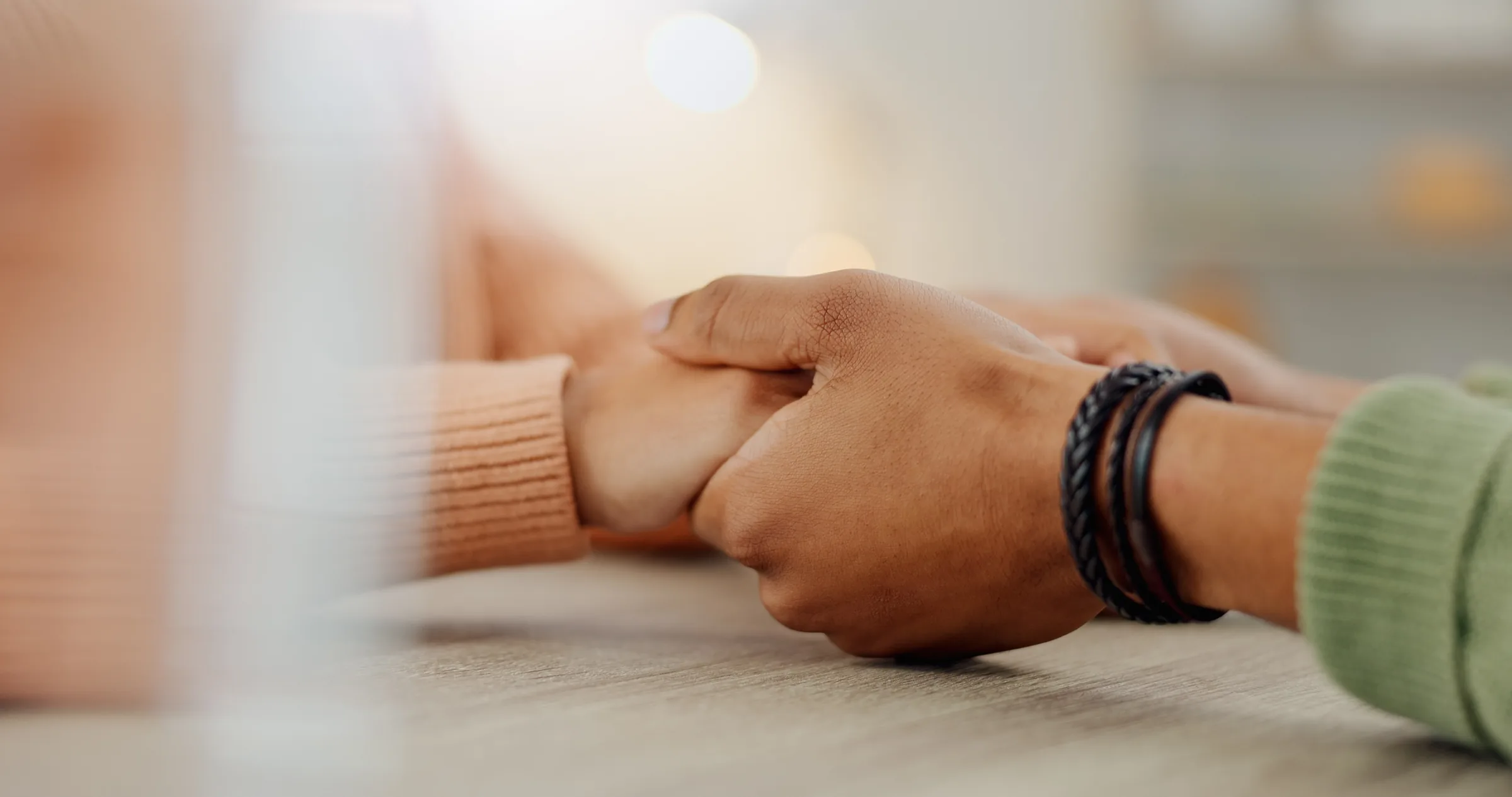 Two people holding hands across a table in a gesture of support.